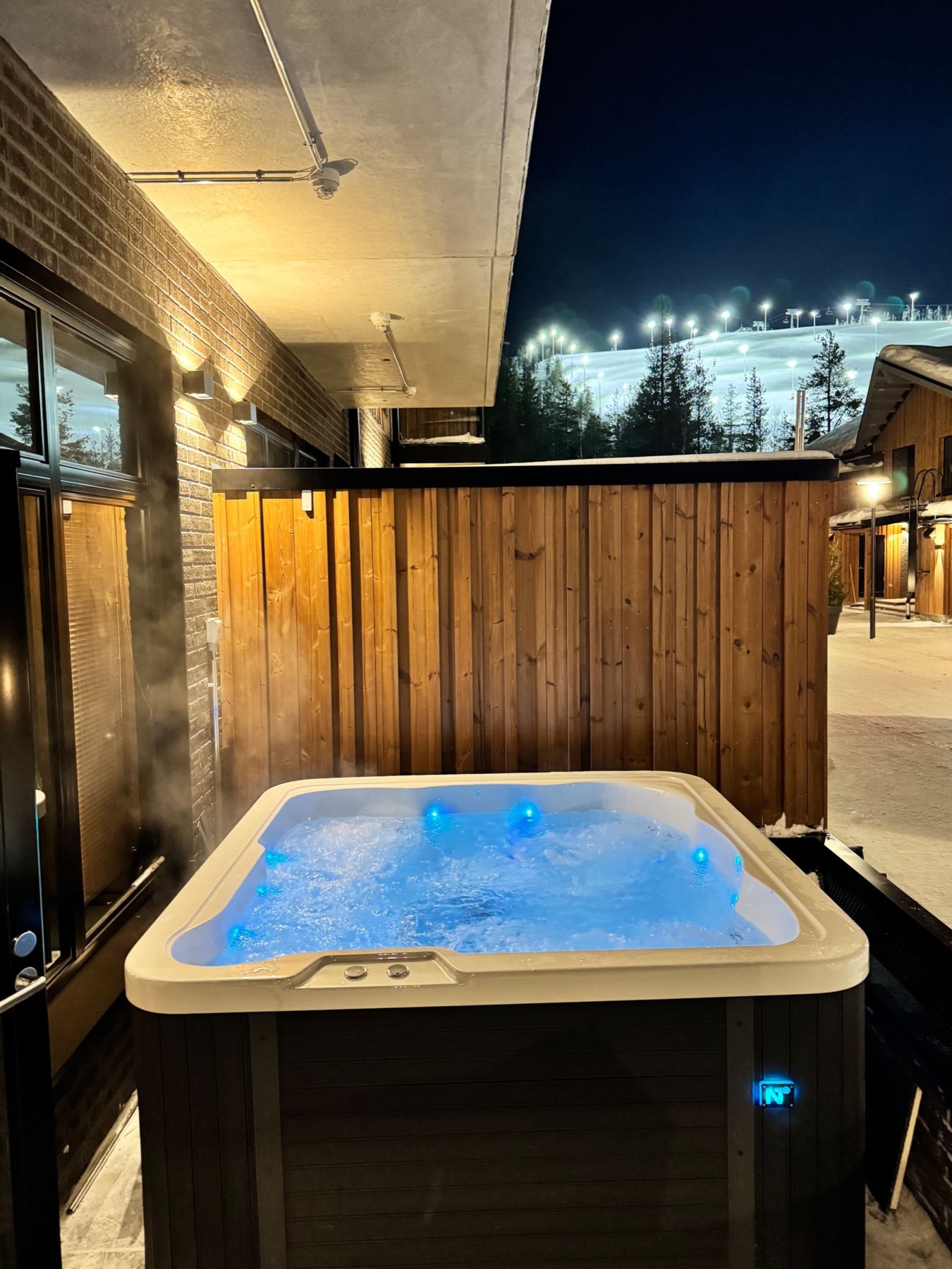 The terrace hot tub at night, steaming, with the floodlit slope behind