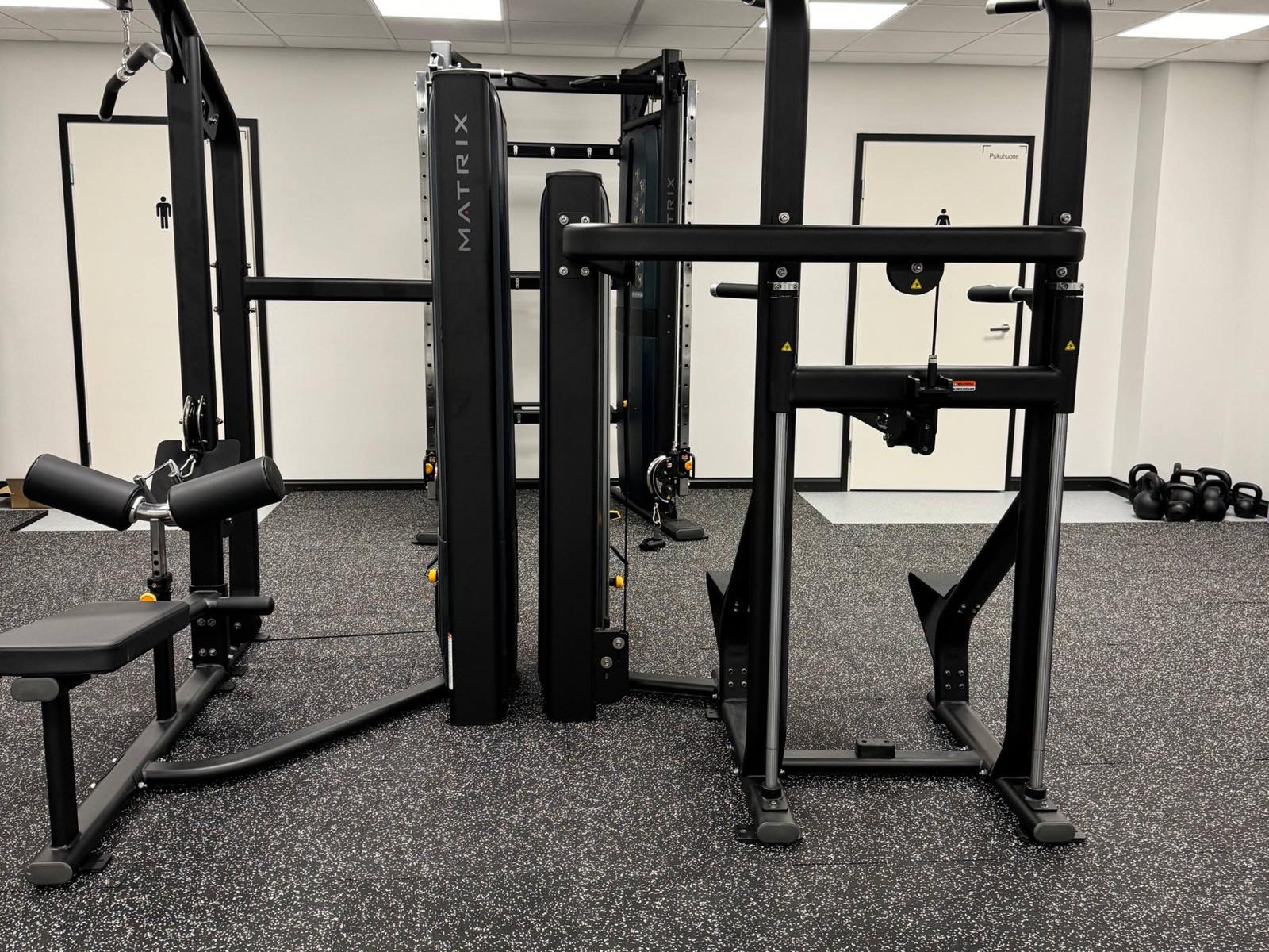 A cable machine and a pull-up and dip station, with kettlebells by the far wall