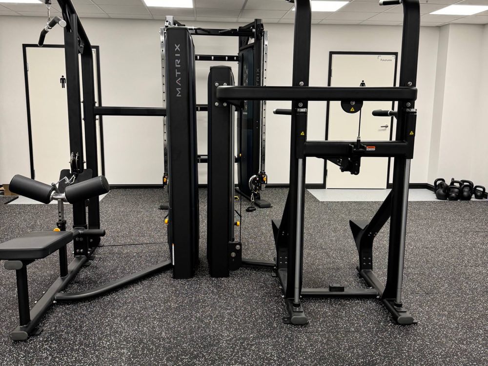 A cable machine and a pull-up and dip station, with kettlebells by the far wall